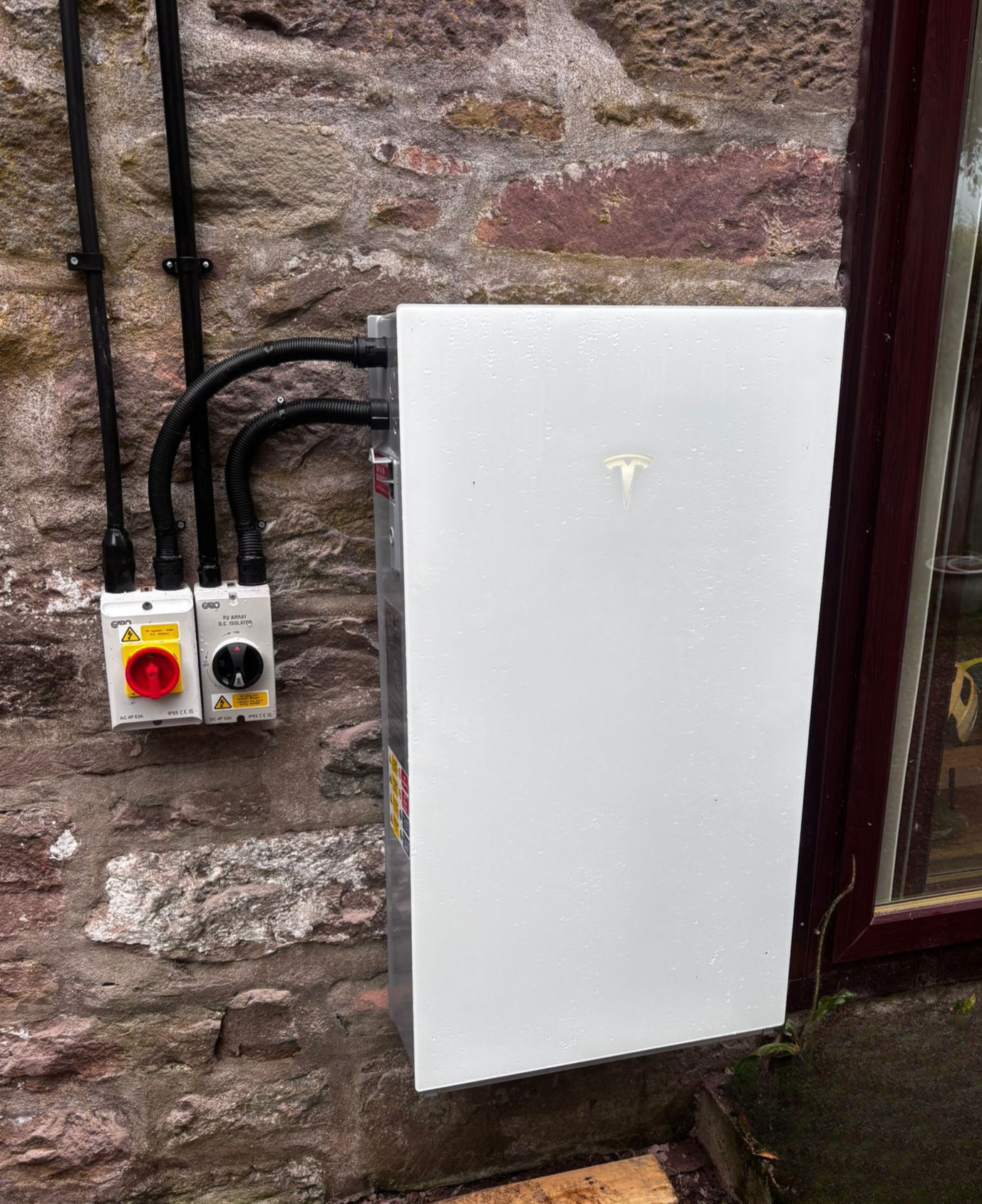 Tesla Powerwall 3 mounted on traditional stone wall with GARO isolators, clean Gensource install